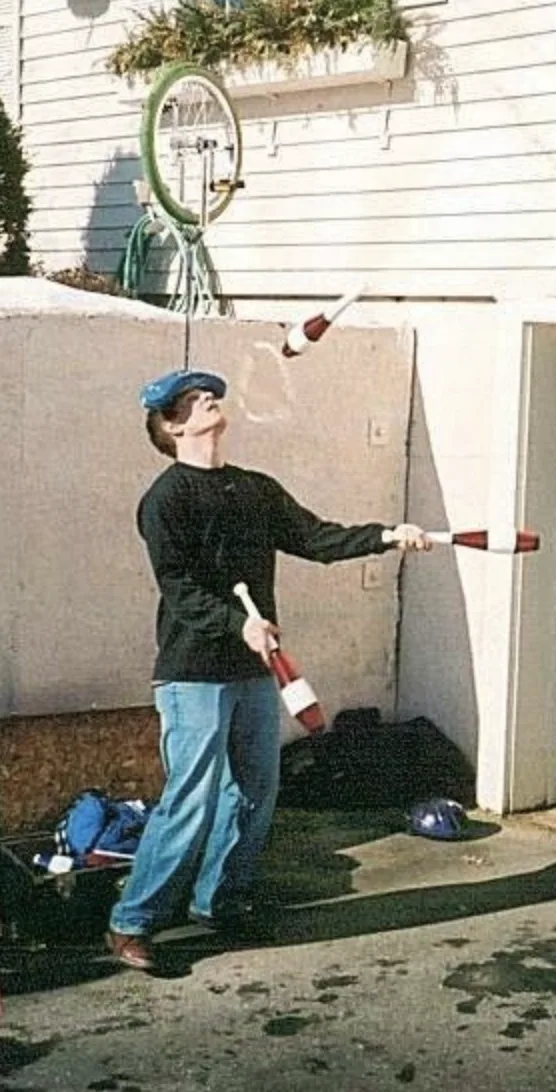 Jacob Abernethy juggling three red-and-white clubs outdoors