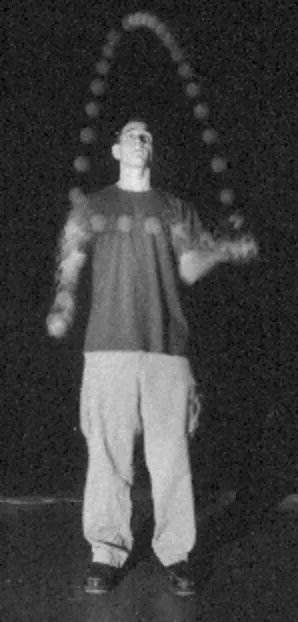 Black-and-white photo of Jacob Abernethy juggling balls onstage beside a microphone